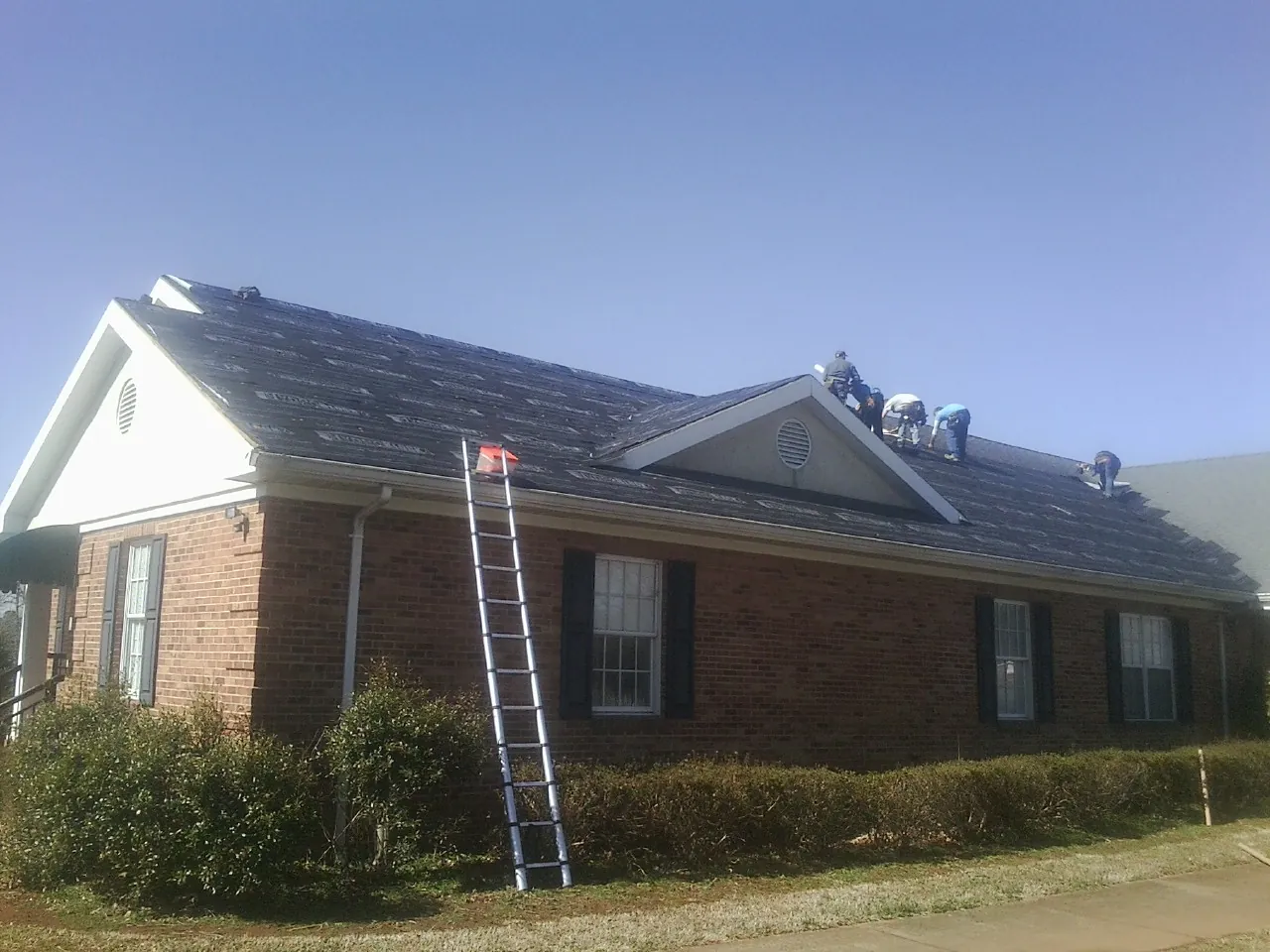 Crew tearing shingles off a brick ranch roof with a ladder set — Emergency Roof Repair work by our crew in Tewksbury