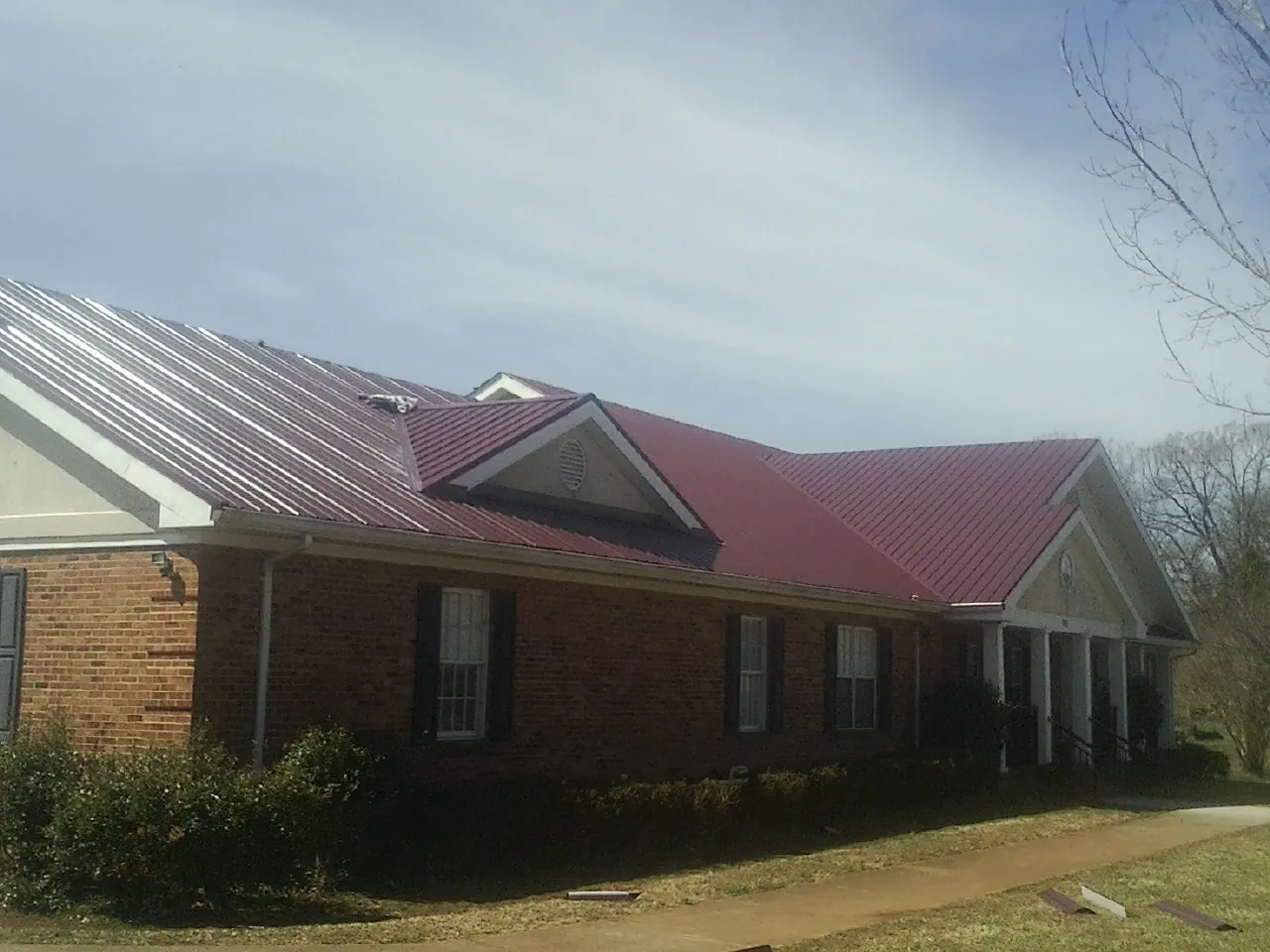 Red metal roof with gabled entries on a long brick building, from a Hail Damage Roof Repair job in Tewksbury