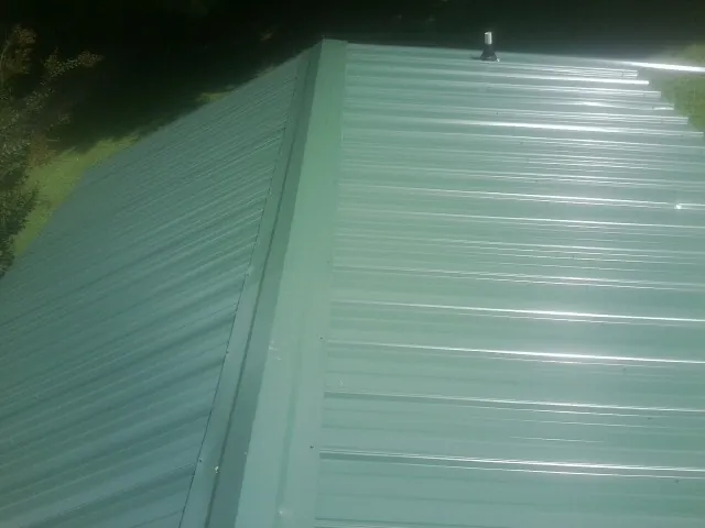 New green metal panels meeting at the ridge of a roof — Flat Roof Repair work by our crew in Tewksbury
