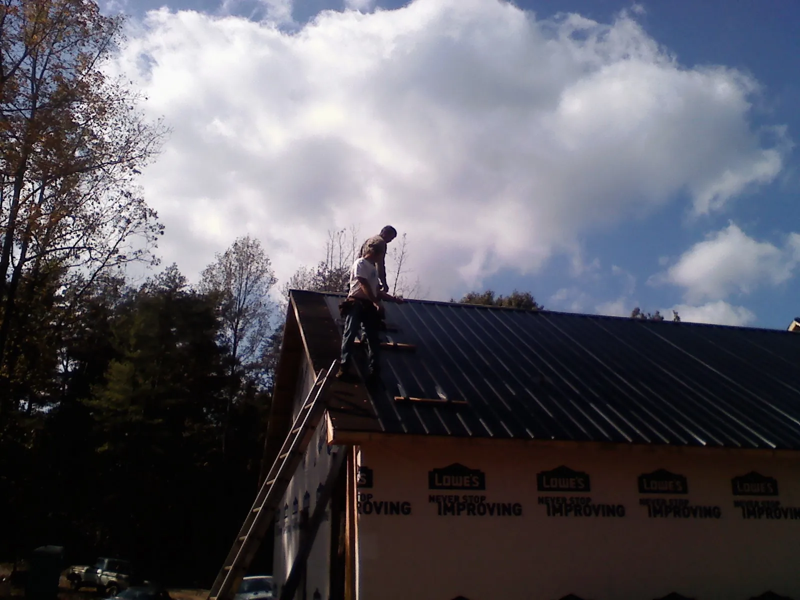 Roofer fastening dark metal panels high against a cloudy sky, from a Roof Inspection job in Tewksbury