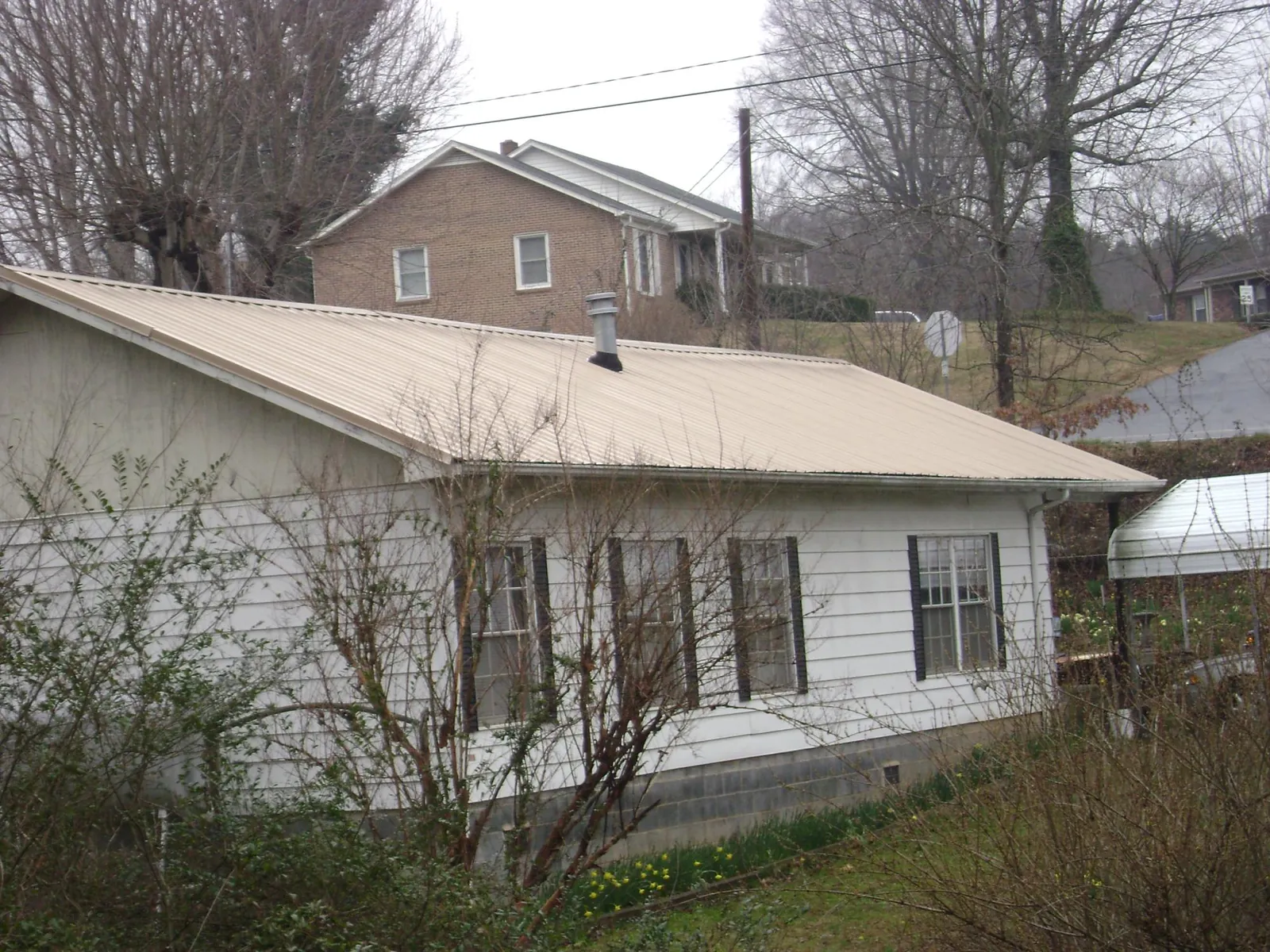 Tan metal roof on a white sided house set into a hillside — Commercial Roofing by Roofing Brothers in Tewksbury