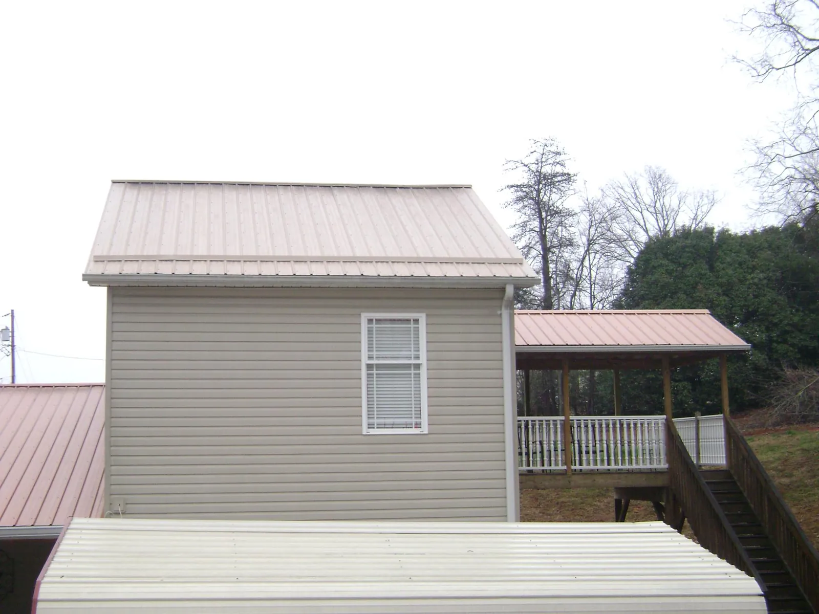 Tan metal roofs on a two story addition and attached porch, from a Roof Replacement job in Tewksbury